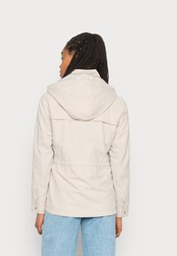 Chaqueta con capucha de color beige claro con cintura ceñida y puños abotonados, hecha de un tejido duradero, con un diseño simple y un detalle mínimo.