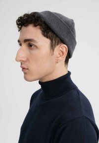 Grijze gebreide beanie gedragen met een donkerblauwe turtleneck. De beanie heeft een snug fit en een geribbelde textuur, met een gladde, lichte stof.