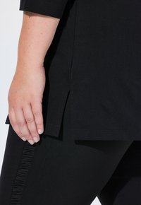 Czarna tunika o prostym kroju z bocznymi rozcięciami, zestawiona z czarnymi legginsami z marszczeniem wzdłuż bocznego szwu.