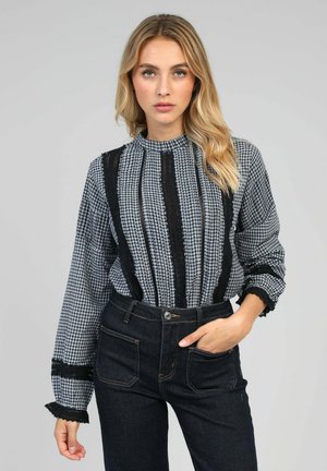 Blouse à motif vichy gris et noir avec un col montant, des manches longues et des détails en dentelle. Associée à un jean en denim foncé taille haute.