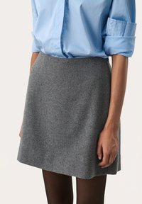 Grå flannel nederdel med A-linje silhuet, parret med en lyseblå button-up skjorte, båret med sorte strømpebukser.