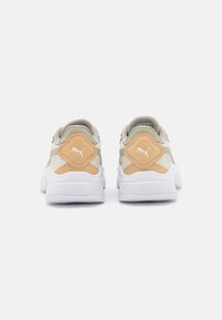 Baskets blanches avec des accents beige et gris. L'arrière présente un panneau texturé avec un logo, un col rembourré et une semelle en caoutchouc design.