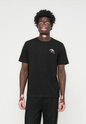 T-shirt en coton noir avec un col rond et des manches courtes. Le côté gauche de la poitrine affiche un design graphique avec des accents rouges et gris.