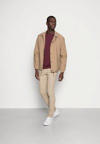 Béžová ľahká bunda s golierom, pod ňou vínová košeľa, béžové priliehavé nohavice a biele tenisky. Jednoduchý, ležérny outfit.