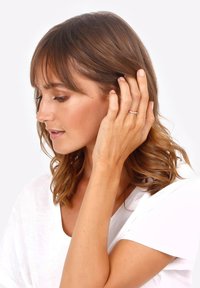 Anello in oro rosa con un design intrecciato, indossato sulla mano sinistra. Il modello ha i capelli castani alla spalla e indossa una camicia bianca.