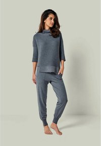 Grau gestrickter übergroßer Pullover mit hohem Kragen, kombiniert mit passenden Jogginghosen. Beide Teile haben eine gerippte Textur und Bündchen.