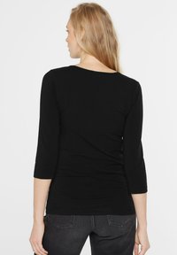 Schwarzes, tailliertes Langarmoberteil mit rundem Ausschnitt und Dreiviertelärmeln, aus weichem, dehnbarem Stoff gefertigt. Einfaches und nahtloses Design.