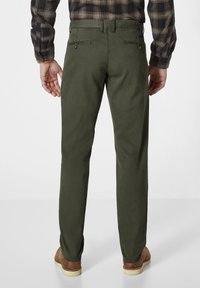 Dark green chinos with a slim fit, featuring rear pockets and button accents. Smooth fabric texture, worn with brown shoes.