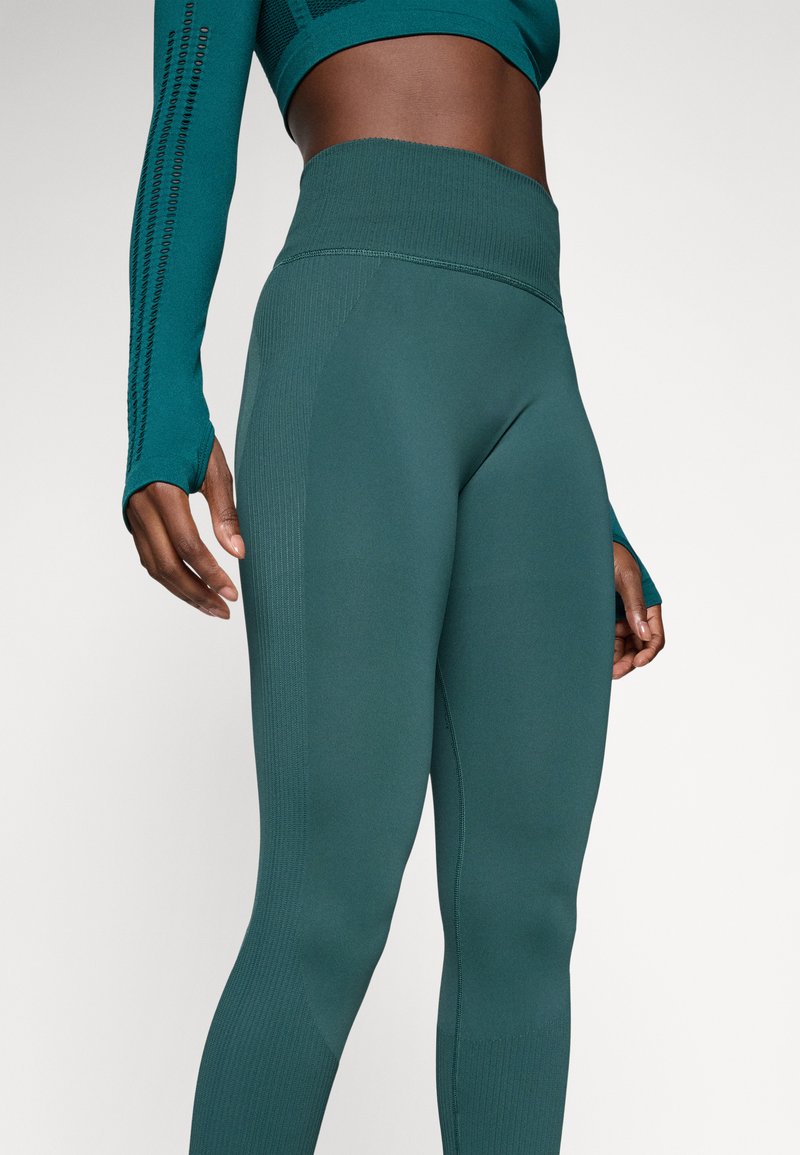 Leggings deportivos en color verde azulado con una cintura alta, textura acanalada y un diseño ajustado. Los detalles en las costuras laterales proporcionan una apariencia estilizada.