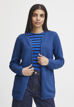 Sininen neulecardigan, jossa on kuvioitu pinta, auki oleva etuosa ja kaksi etutaskua. Päällä sinivalkoraidallinen paita.