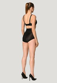 Zwart lingerieset met een strakke beha met verstelbare bandjes en hoge doorschijnende slipjes. Het model draagt zwarte hoge hakken.