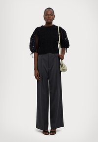 Černý top s krátkým rukávem s texturovanou krajkou a květinovými detaily, spárovaný s šedými kalhotami s vysokým pasem a širokými nohavicemi a černými sandály.