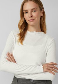 Weißes, geripptes Langarmtop mit gewelltem Ausschnitt und kleinen silbernen Punktemustern. Weicher Stoff, taillierte Passform für einen eleganten Look.