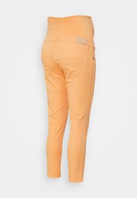 Calças com cintura elástica laranja, de corte ajustado, com dois bolsos traseiros e uma textura suave. Comprimento cropped, sem hardware visível.