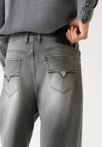 Šedé džínsy z denimu s úzkym strihom, ktoré majú dve zadné vrecká, trojuholníkovú nášivku a detaily s kontrastným prešívaním.