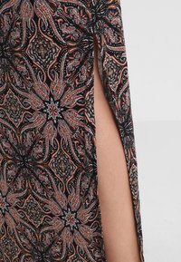 Tela negra con patrones que presentan diseños intrincados en rojo, naranja y gris. La prenda tiene aberturas laterales y un acabado texturizado.