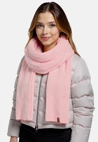 Bufanda de punto rosa con textura de canalé, llevada suelta alrededor del cuello, combinada con una chaqueta acolchada gris claro y una camiseta negra.
