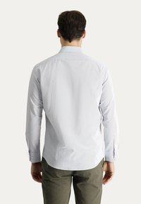 Lichtblauwe lange mouwen shirt met een klassieke kraag, voorzien van een gestructureerde stof, knoopmanchetten en een gebogen zoom. G gedragen met olijfgroene broek.
