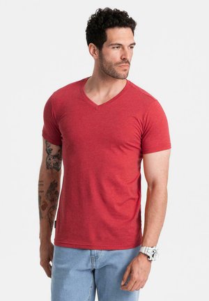 Camiseta de algodón roja con cuello en V y mangas cortas, que presenta un ajuste casual y una textura suave. Se lleva con jeans de mezclilla azul claro.