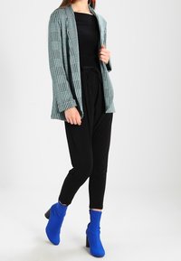 Rutigt kavaj i teal och svart, matchat med en svart topp och svarta byxor. Utrustad med blå ankelstövlar och en strukturerad tyg.