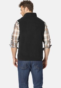 Schwarze Fleece-Weste mit hohem Kragen, getragen über einem karierten Hemd. Verfügt über eine glatte Textur und ein schlichtes Design. Jeans aus Denim sind darunter sichtbar.