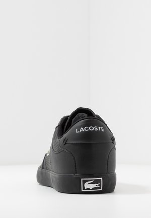 Baskets noires Lacoste montrant le côté arrière avec le texte blanc Lacoste sur le talon et le logo crocodile blanc sur la semelle.