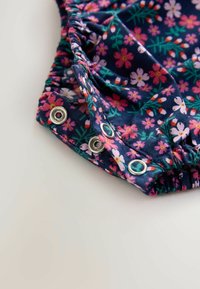 Blumendruckstoff in Marineblau mit rosa und grünen Akzenten. Verfügt über elastische Rüschen und metallene Druckknopfverschlüsse mit Ösen.