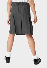 Grijze geplooide rok met een elastische tailleband, gecombineerd met zwarte lakleren schoenen en witte gerimpelde sokken.