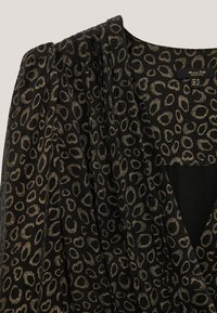 Tissu noir avec des motifs circulaires dorés, arborant des drapés et un décolleté en V profond. Étiquette visible à l'intérieur du vêtement.
