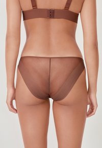 Mutande trasparenti marroni con una texture liscia e una copertura minima. Presentano sottili cinturini laterali e un design della parte posteriore senza cuciture.