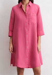 Różowa, lniana sukienka koszulowa z zapięciem na guziki z przodu, kołnierzykiem i kieszenią. Posiada długie rękawy z podwiniętymi mankietami oraz boczne rozcięcia dla łatwości ruchu.