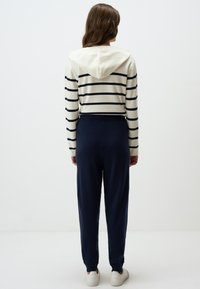 Sweat à capuche rayé blanc et marine associé à un jogging marine. Tissu lisse, coupe décontractée, taille élastique et chevilles resserrées.