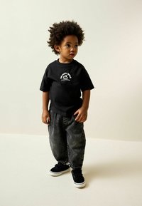 Black cotton t-shirt with white text and graphic design, paired with loose grey denim pants and black sneakers with white sole.