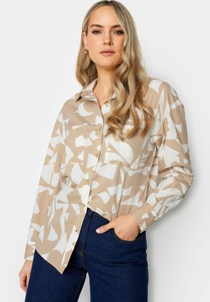 Camicia beige con bottoni, decorata con motivi astratti bianchi, maniche lunghe e colletto classico. Abbinata a jeans in denim scuro.