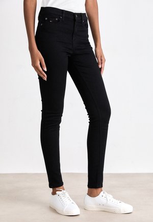 Jean skinny noir taille haute en denim, avec un design classique, cinq poches et des détails de couture subtils, associés à des baskets blanches.