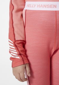 Sportovní oblečení Helly Hansen s texturovaným růžovým tričkem s dlouhým rukávem a bílými pruhy na rukávu, doplněné o těsné kalhoty se značkovým pasem.
