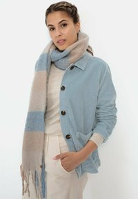 Lichtblauwe corduroy jas met een kraag, gekenmerkt door grote bruine knopen; gecombineerd met een beige en blauw gestreepte sjaal.