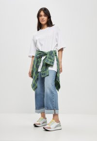 Camiseta blanca de gran tamaño, jeans cortos de color azul claro, camisa de cuadros verdes atada a la cintura, zapatillas deportivas multicolores con cordones.