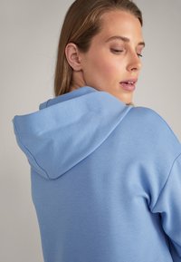 Felpa con cappuccio di colore azzurro chiaro, realizzata in tessuto morbido, con vestibilità comoda e superficie liscia, arricchita da cuciture visibili lungo il cappuccio.