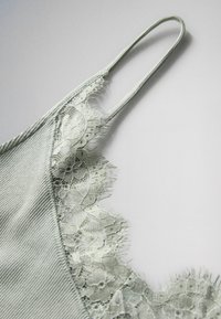 Svetlozelené rebrované tielko s tenkými ramienkami a kvetinovou čipkou pozdĺž výstrihu a hornej časti hrudníka.