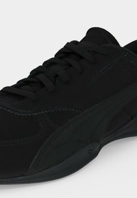 Chaussure de sport noire avec lacets, coutures détaillées et semelle texturée, présentée en angle sur fond clair uni.