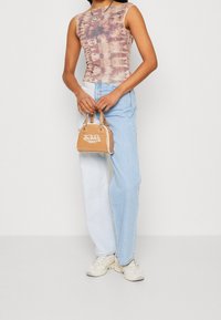Top bez rukávů s batikovaným vzorem v béžových a hnědých odstínech, spárovaný se světlými modrými rovnými džíny. Béžová kabelka s logem a stříbrnou kováním.