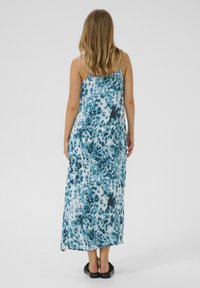 Robe maxi en tissu léger avec un imprimé léopard turquoise et noir. Dotée de fines bretelles et d'une coupe décontractée. Sandales plates portées.