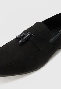 Schwarze Wildleder-Loafer mit glatter Oberflächenstruktur, ausgestattet mit einer dekorativen Lederquaste und einer flachen Gummisohle. Minimale Nähdetails.
