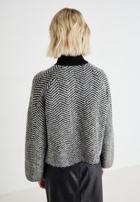 Maglione a motivo pied de poule in bianco e nero con collo alto, maniche lunghe e orlo corto. Texture a maglia morbida.