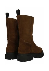 Botas de tobillo de ante marrón con suelas de goma negra gruesa y tiradores, mostradas desde ángulos trasero y lateral sobre un fondo blanco.