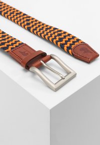 Geweven riem in marineblauw en oranje met tan leren accenten, voorzien van een metalen gesp en een gestructureerd, flexibel ontwerp.
