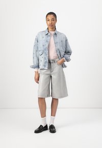 Light blue denim oversized jacket with floral embellishments, paired with light grey denim bermuda shorts and black loafers, worn with white socks.