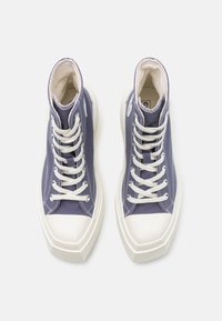 Baskets montantes avec un dessus en textile violet foncé, un embout en caoutchouc blanc et des lacets plats blancs. Semelle blanche épaisse au design angulaire.