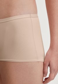 Beige boyshorts gemaakt van glad, rekbaar materiaal, met een laag uitgesneden tailleband en minimale stiksels langs de randen voor comfort.